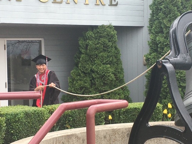 Graduate ringing large outdoor bell with rope