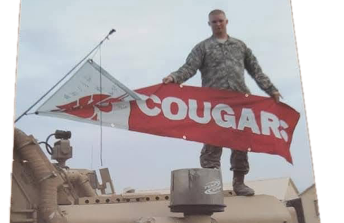 Soldier holding Cougar banner atop military vehicle